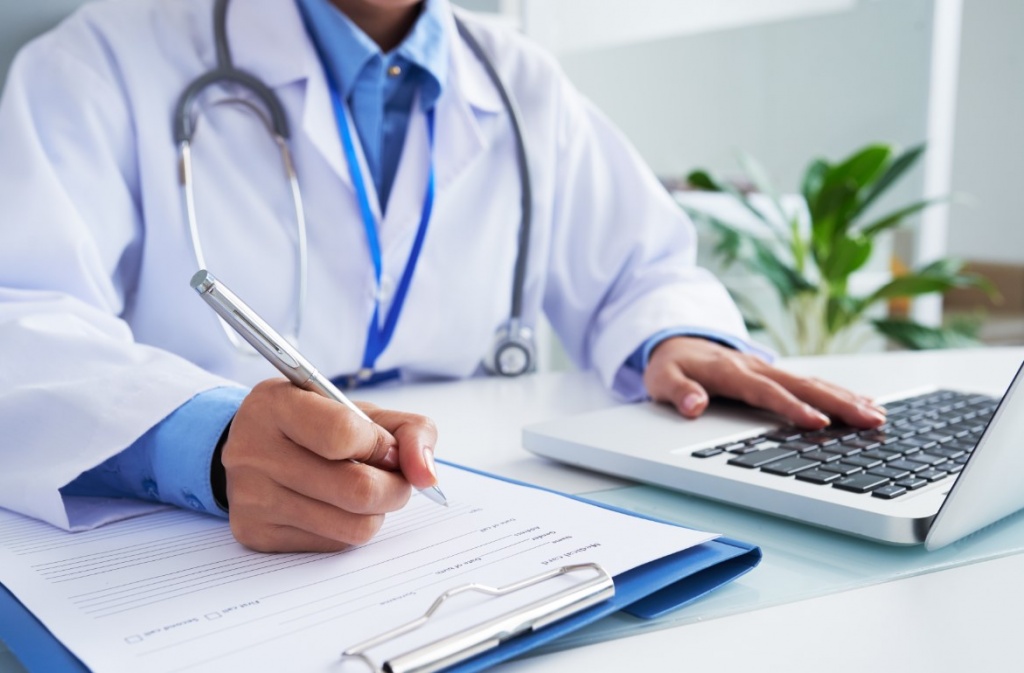 1611676711_hands-unrecognizable-female-doctor-writing-form-typing-laptop-keyboard